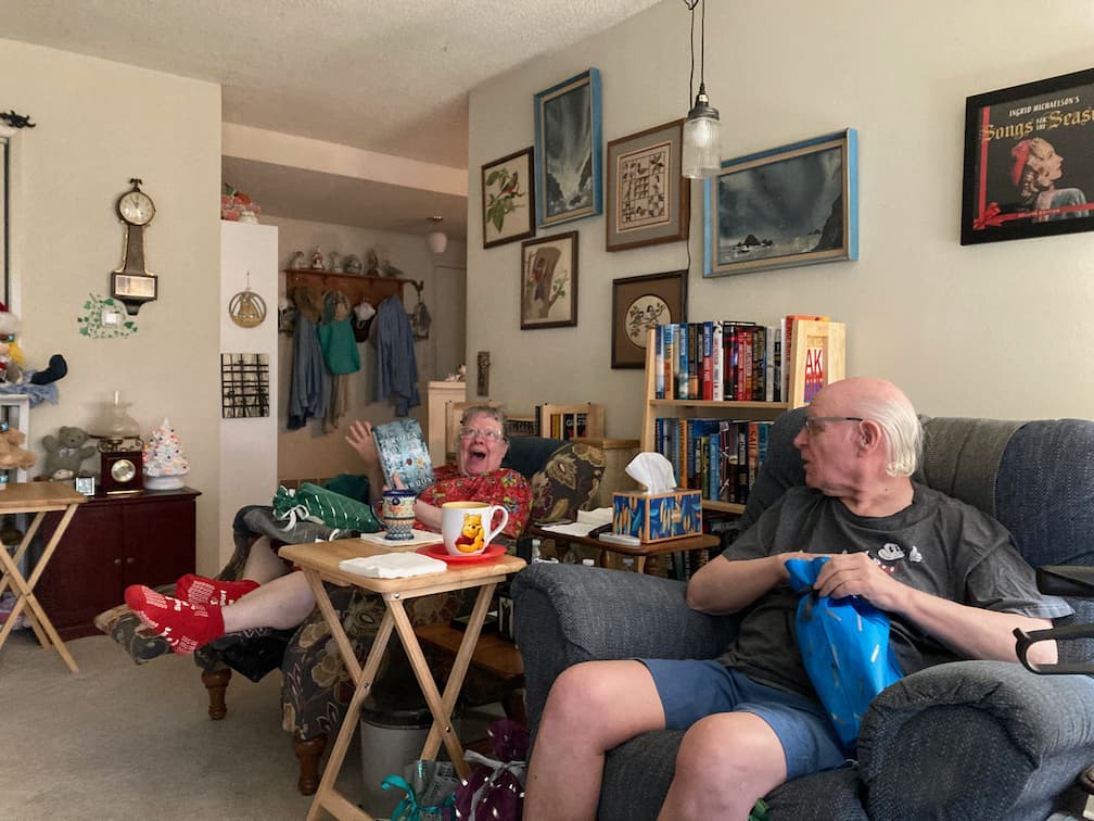 my parents opening gifts and showing off gifts. My mom is showing an almost sarcastic level of joy at this book, a copy of The Frozen River by Ariel Lawhon, which my dad thought would sound interesting to her.